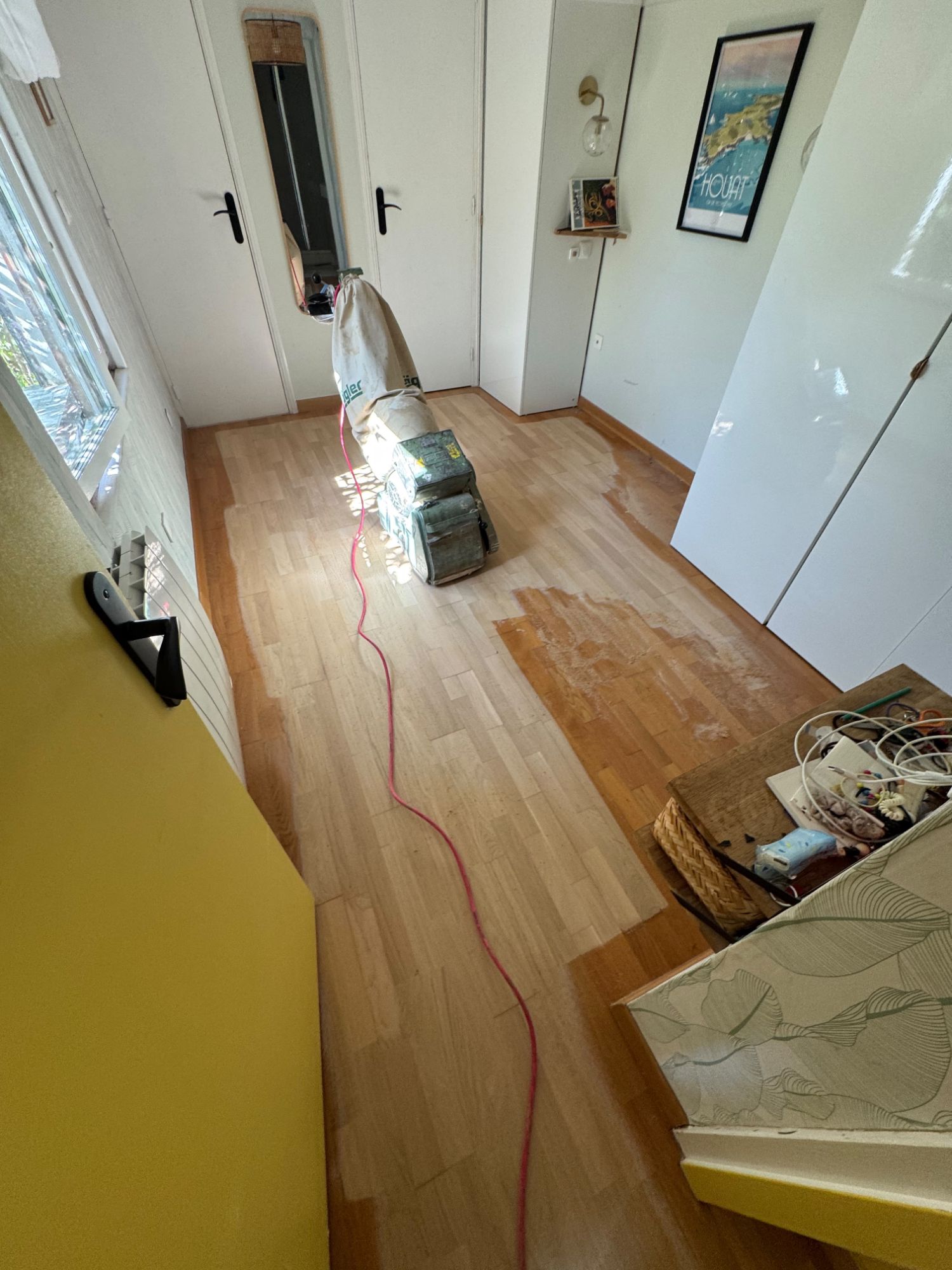 Ponceuse à bande en cours de passage sur un parquet en chêne, zone poncée à vif