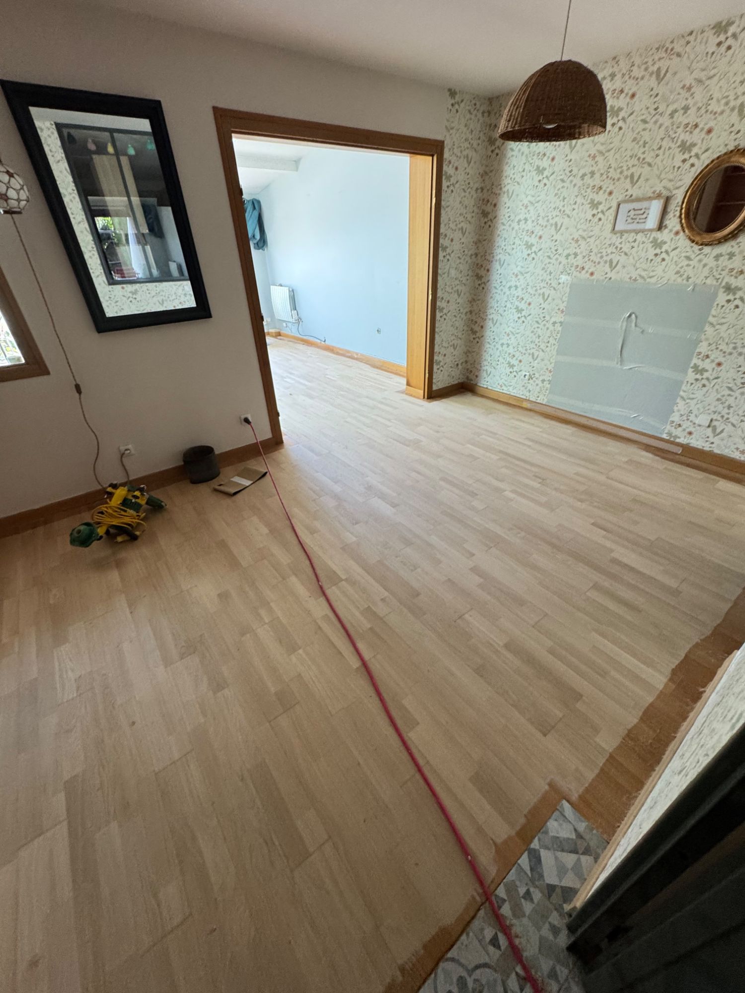 Ponceuse de bord et rallonge posées sur un parquet en cours de ponçage